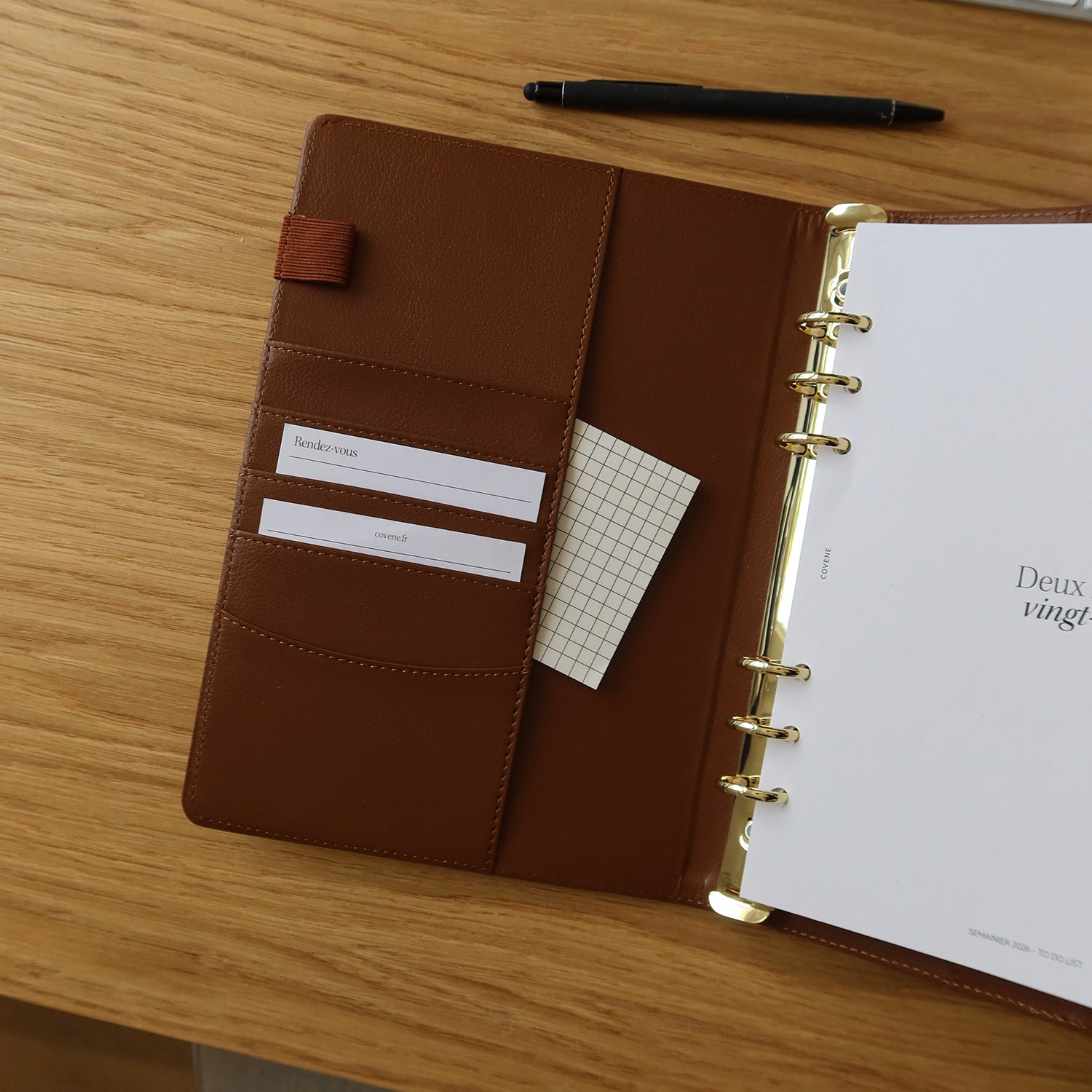 agenda couverture à 6 anneaux, posé sur un bureau avec un crayon et des écouteurs sans fils. Couverture anneaux pour composer soi même son agenda selon ses besoins