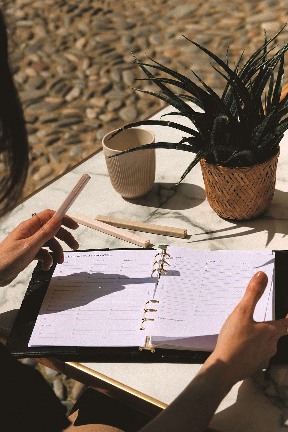 terrasse d'un café, table en marbre, feutres surligneurs pastels, agenda ouvert, A5 recharges anneaux 6, plante