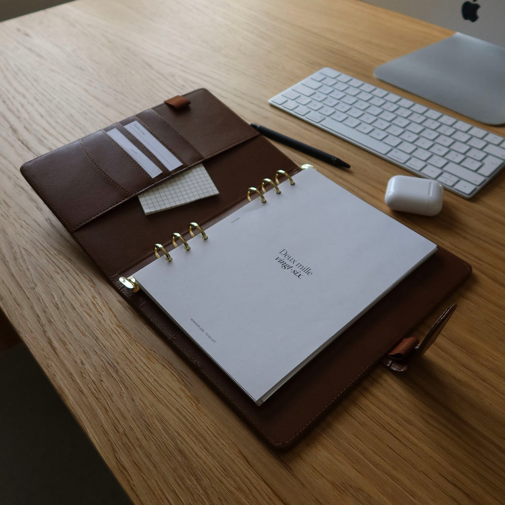 agenda couverture à 6 anneaux, posé sur un bureau avec un crayon et des écouteurs sans fils. Couverture anneaux pour composer soi même son agenda selon ses besoins